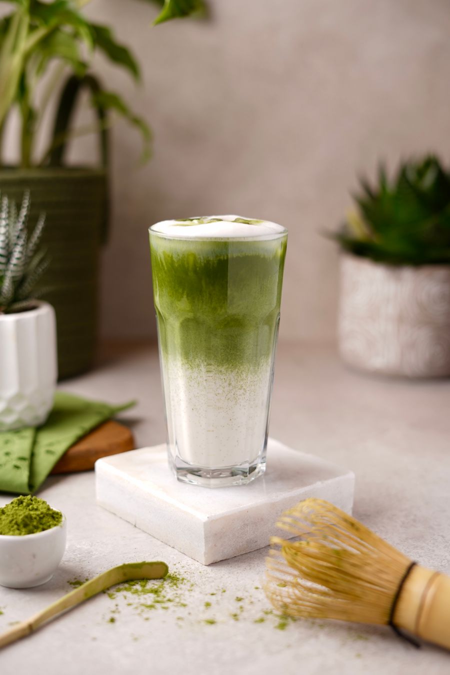 Iced matcha latte beside a bamboo whisk and matcha powder
